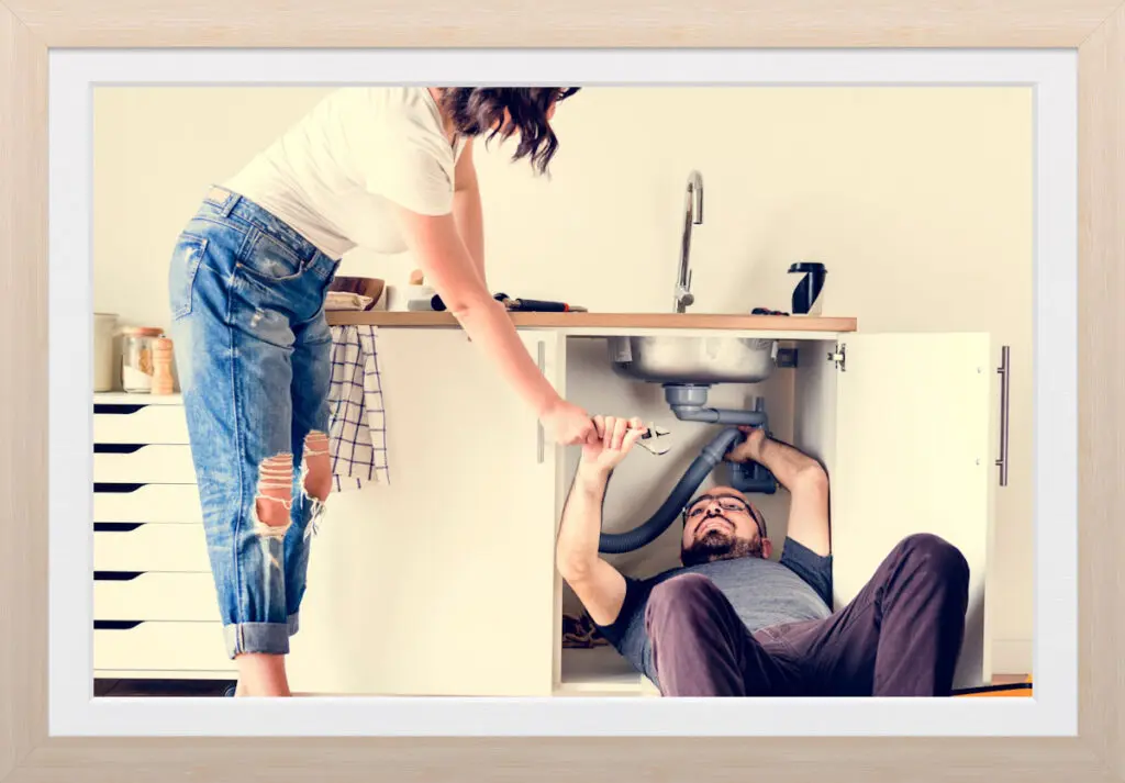 Framed photo of two people working together to repair a kitchen sink.