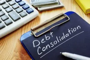 Debt consolidation written on clipboard sitting on desk with calculator and cash.