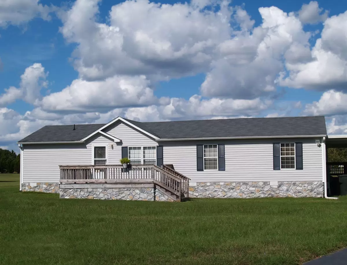 Gray manufactured mobile home with stone skirting sitting on nice grass with blue sky.