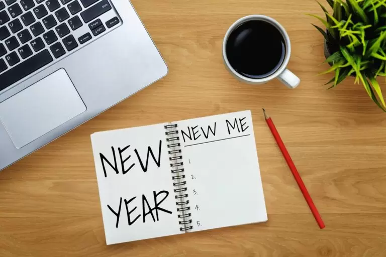 New Year New Me resolution written on notepad on coffee table with laptop, pencil and plant.