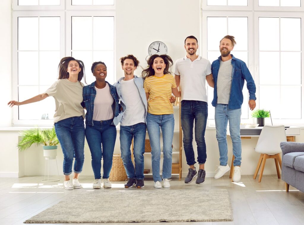 Diverse group of happy homeowners jumping in a bright living room representing successful home improvement loan borrowers.