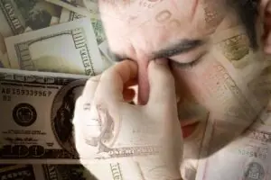 Person looking distressed while holding their head, surrounded by money, illustrating the link between mental health and financial struggles.