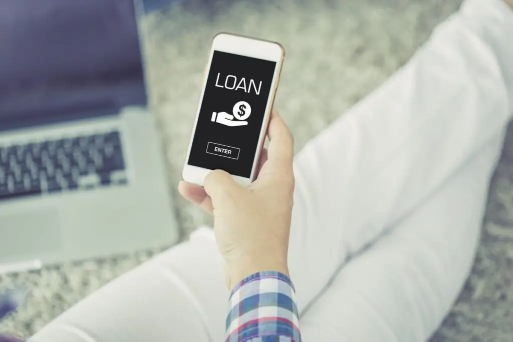 A person sitting on the floor using a smartphone to research low APR personal loans.