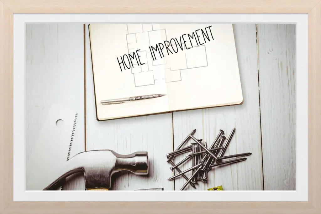 Framed photo of the words "home improvement" on wood flooring surrounded by tools.