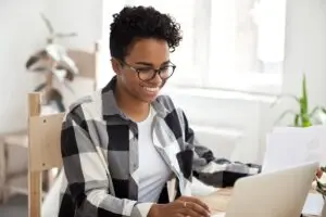 Smiling person at a laptop researching 25 proven ways to borrow 500 dollars fast.