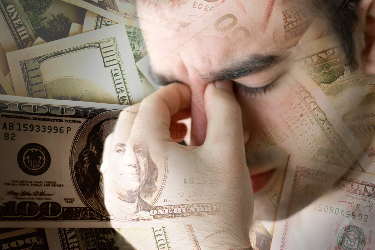 Stressed young man holding his face with money all around.