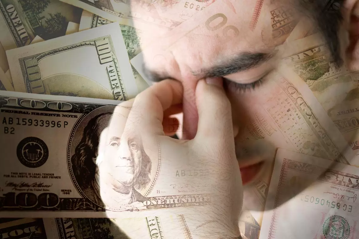 Stressed young man holding his face with money all around.