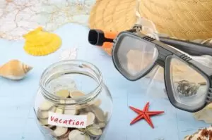 Vacation money jar on the world map with shells, hat, and goggles.