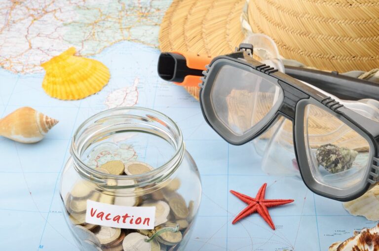 Vacation money jar on the world map with shells, hat, and goggles.